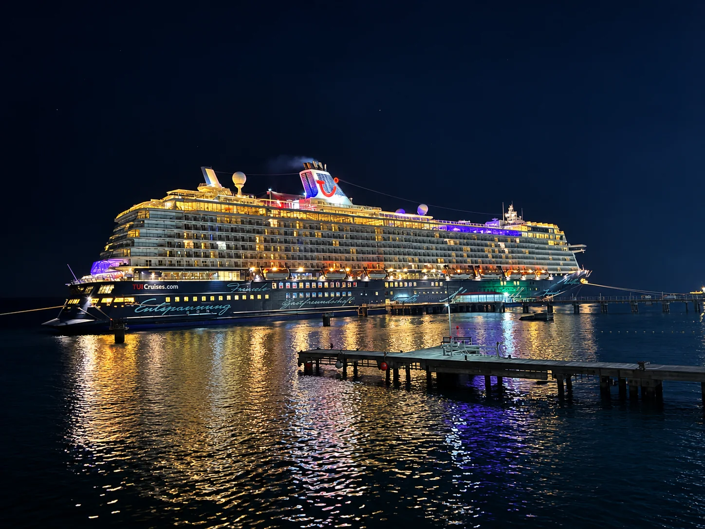 An illuminated cruise ship in the harbour at night, with lights reflected on the water