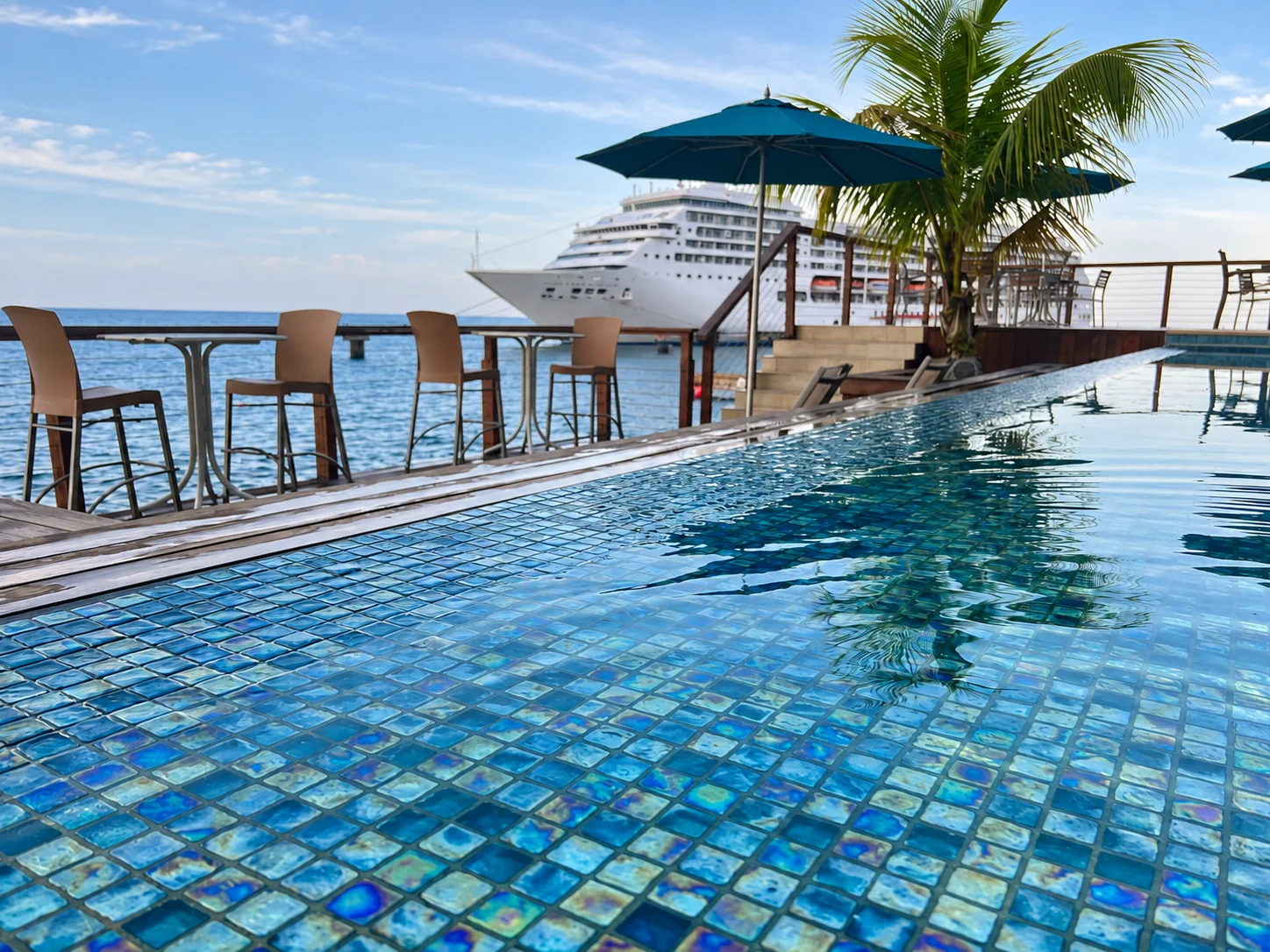 A seaside pool with a palm tree and a ship in the distance
