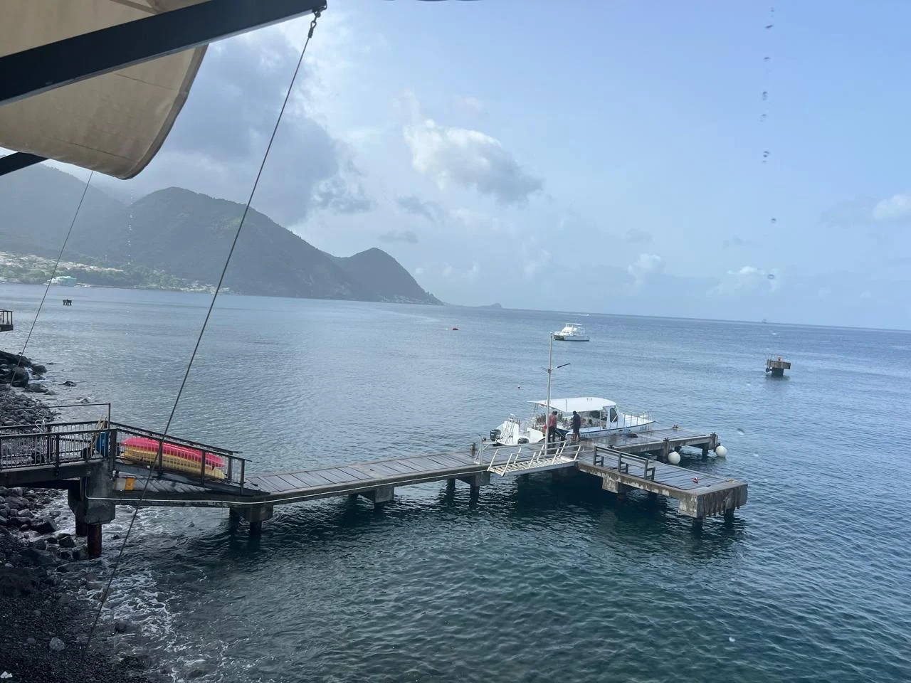 A wooden jetty and boat overlooking the sea and a green mountain headland