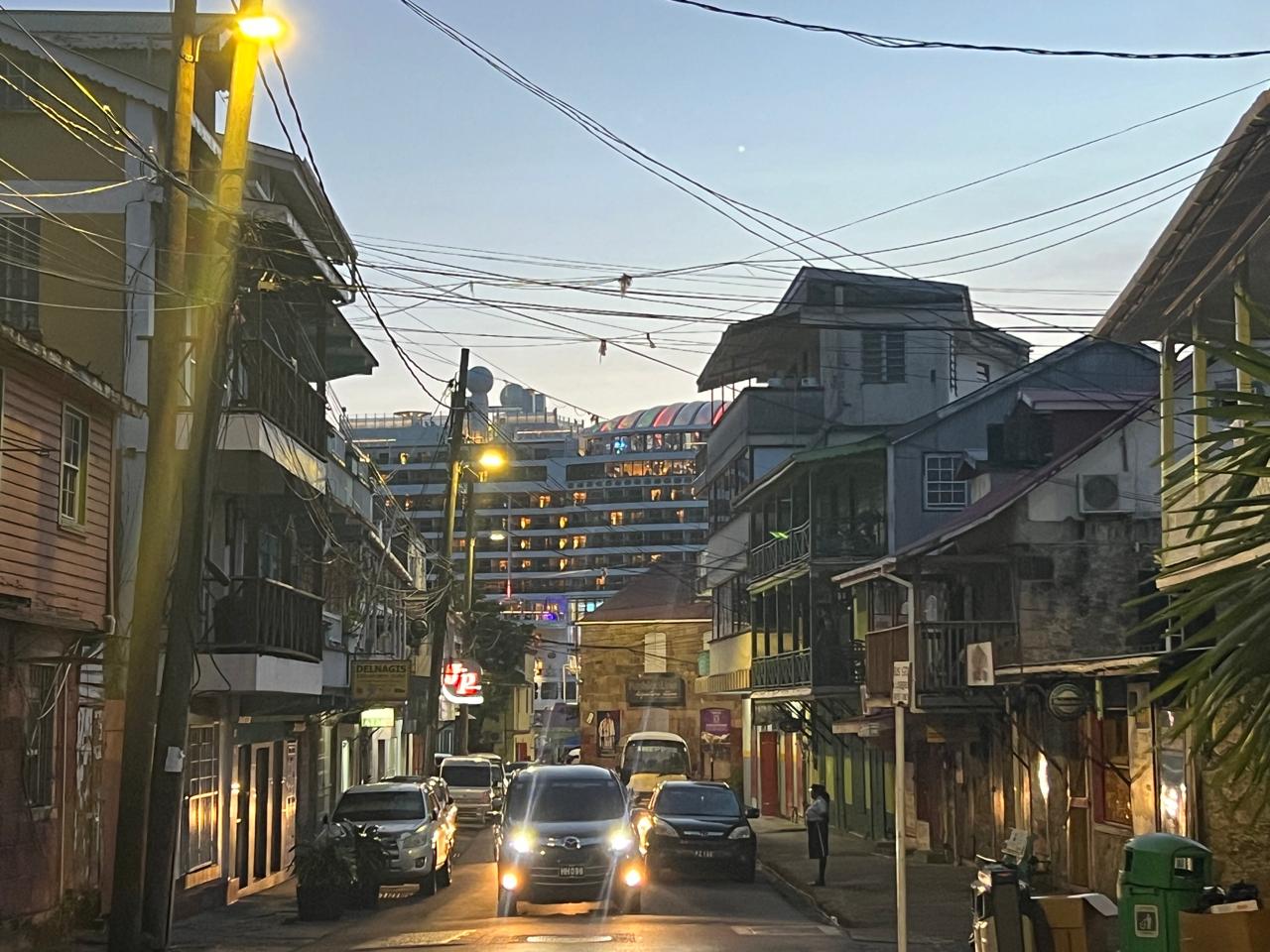 An evening street with wooden balconies and a ship in the distance